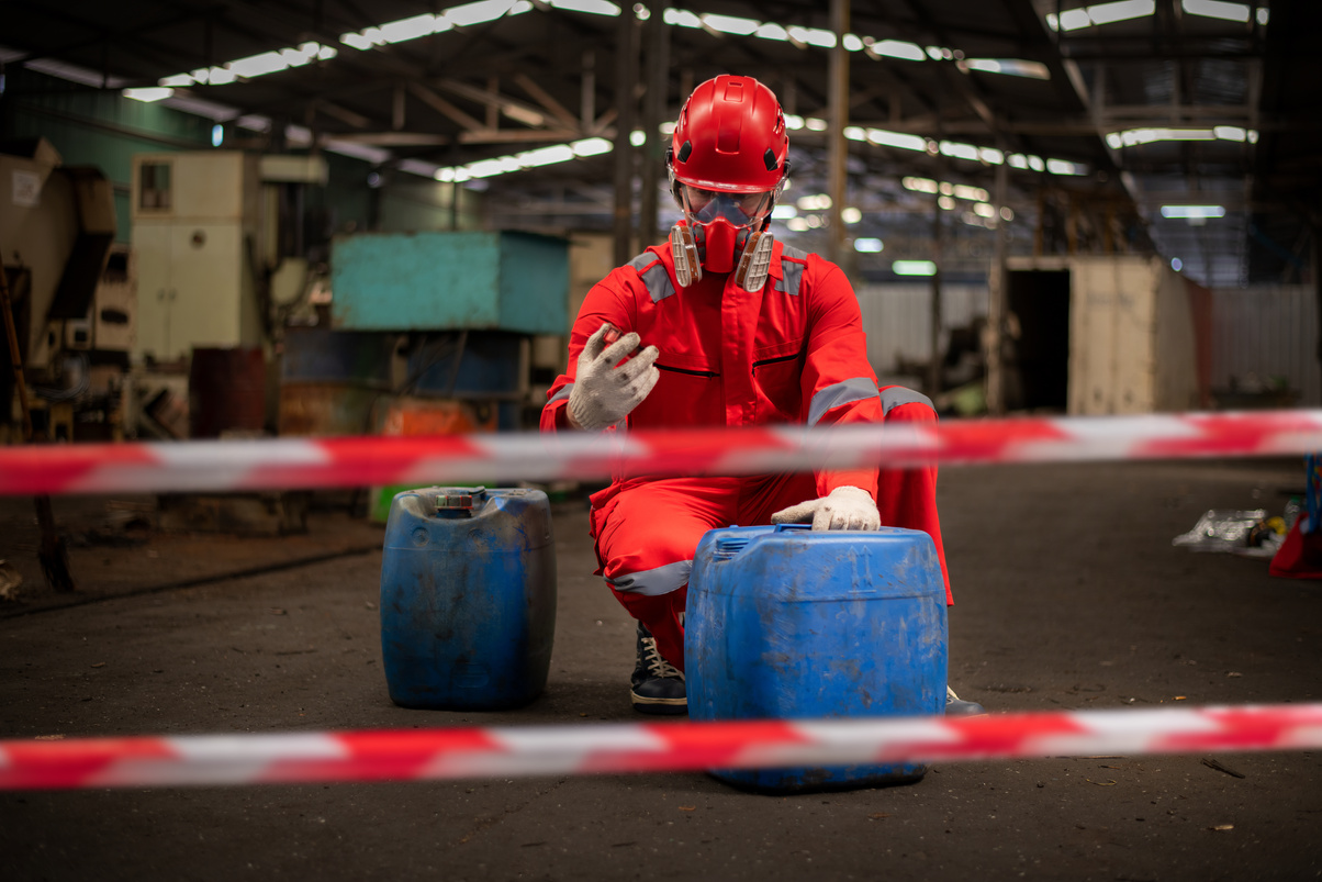 Worker wearing safety uniform and gas mask they used stretching the red white warning tap in spilled oil .Red and white Hazardous restricted area factory is safety worker industry concept.